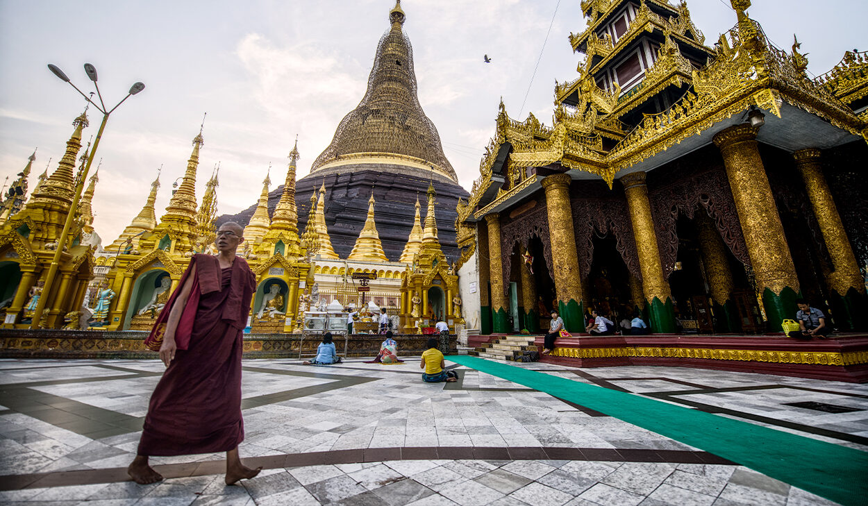 A Buddhist man walks through the courtyard of a temple in Southeast Asia.