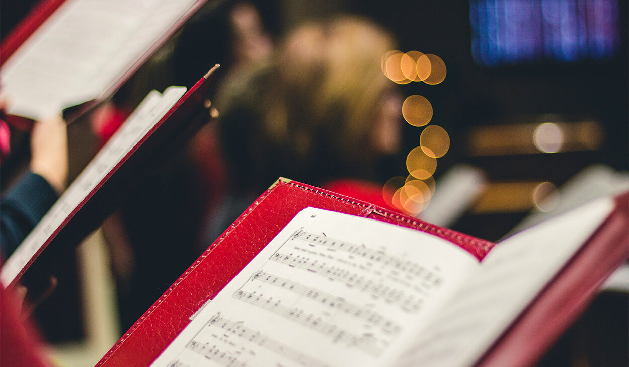 A choir is seen holding sheet music in red folders.