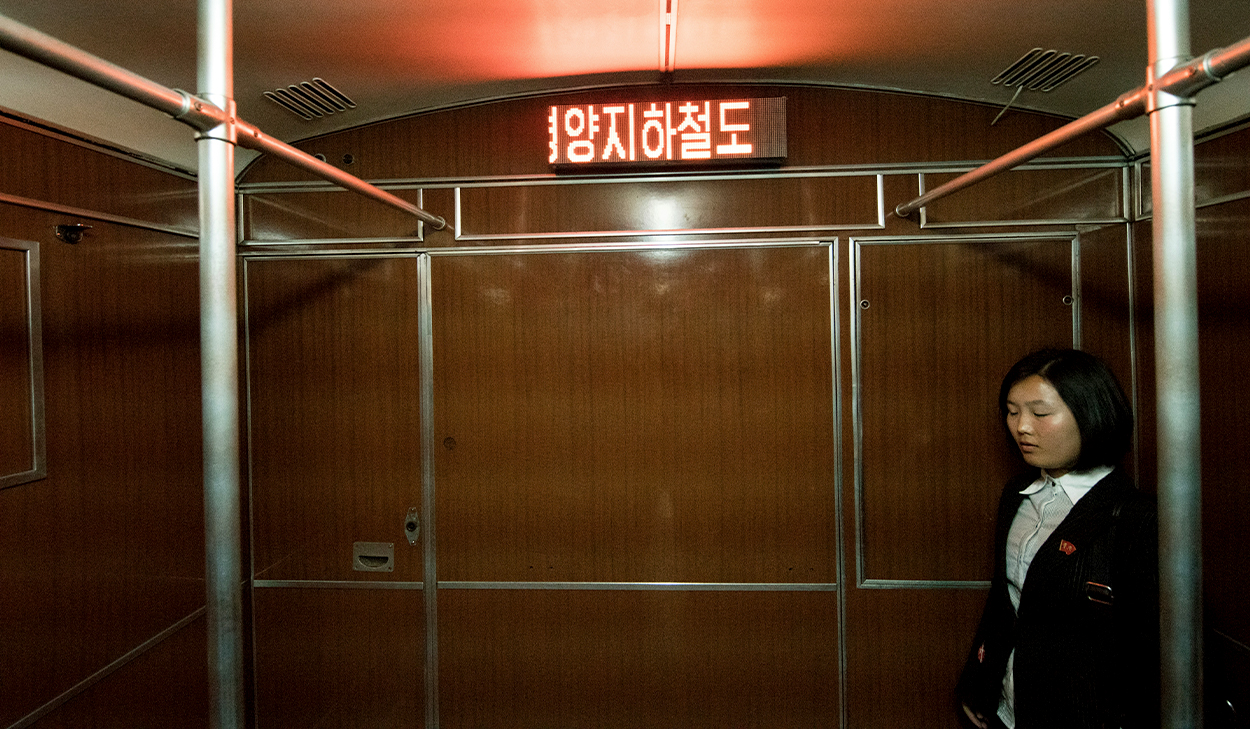 A woman with short hair stands alone on a metro train in North Korea.