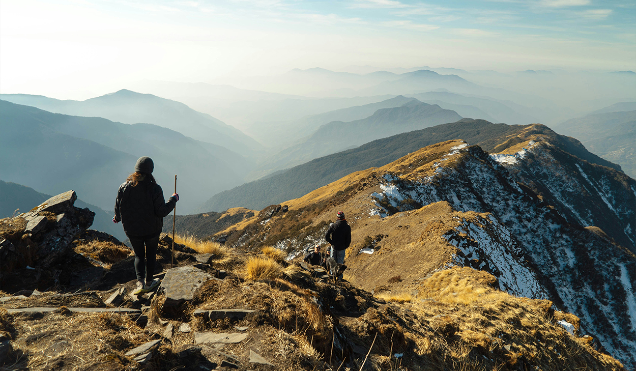 Two people in hiking gear trek through mountains.