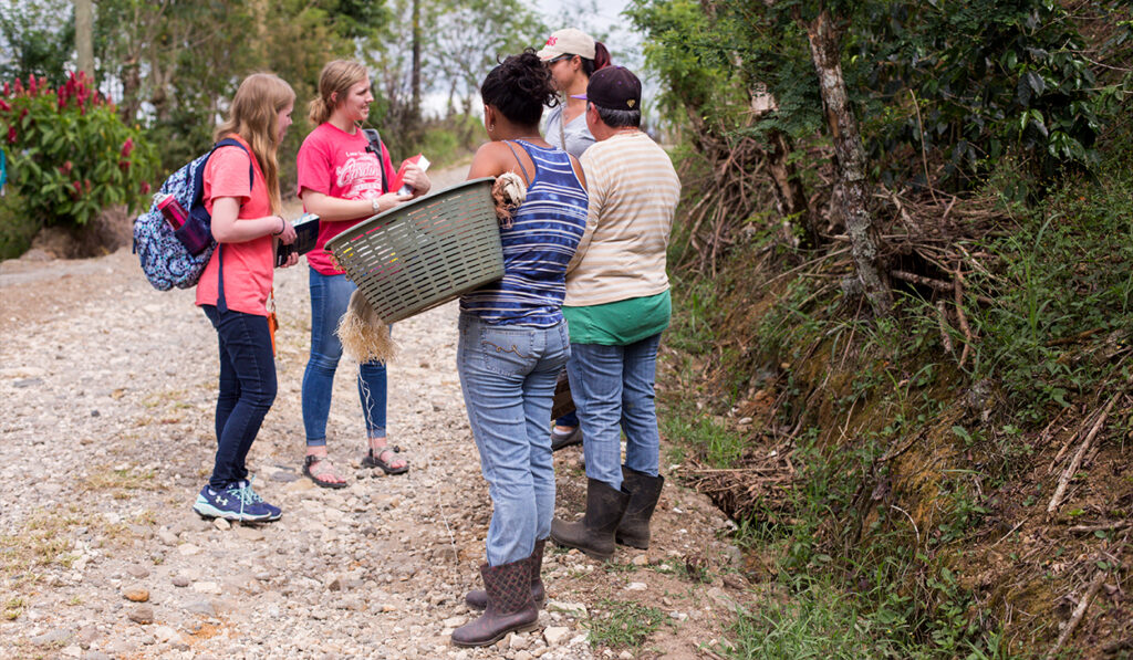 A couple of high school girls talk to a group of women in Latin America on a dirt road.