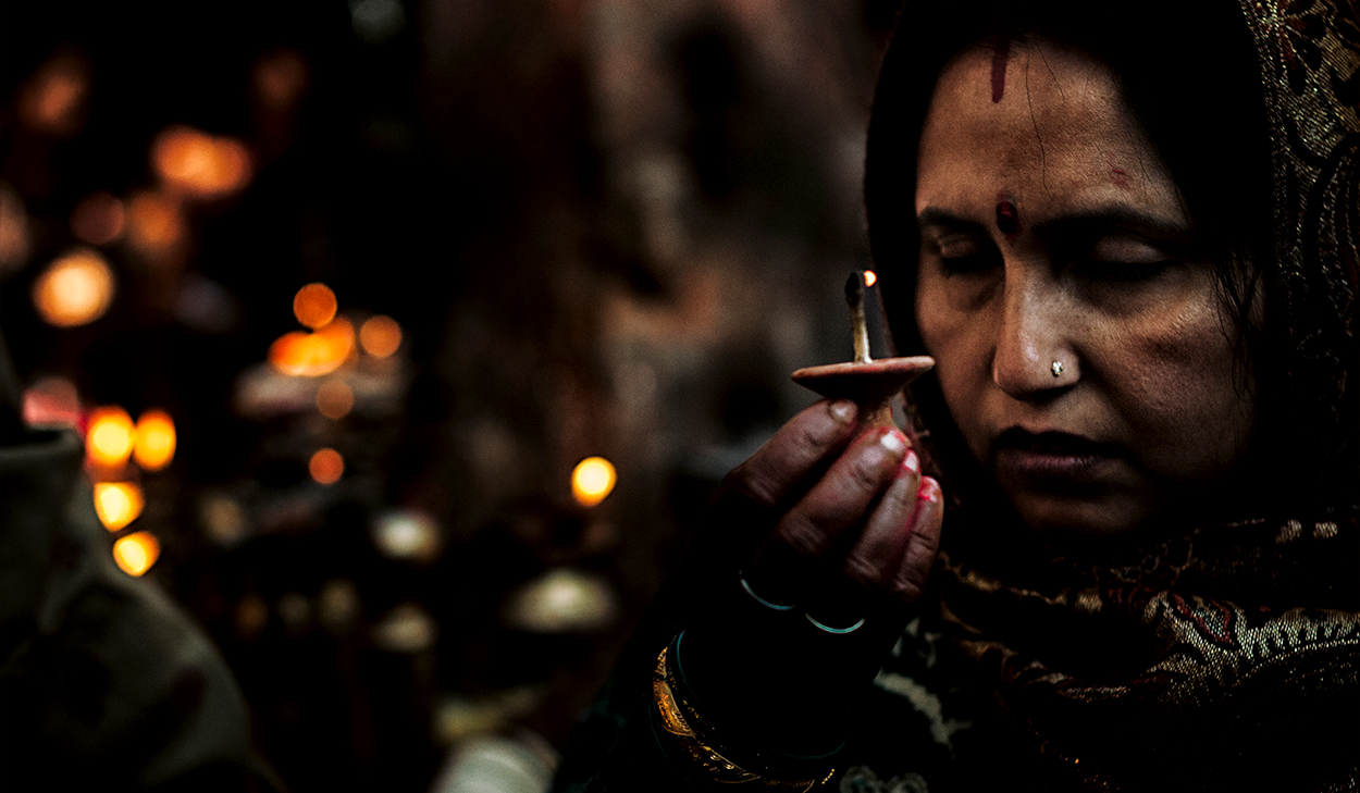 A Hindu woman with her eyes closed holds up an oil lamp.