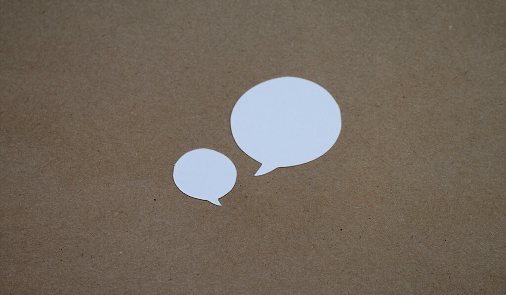Two speech bubbles cut out from white paper are set on top of brown paper.