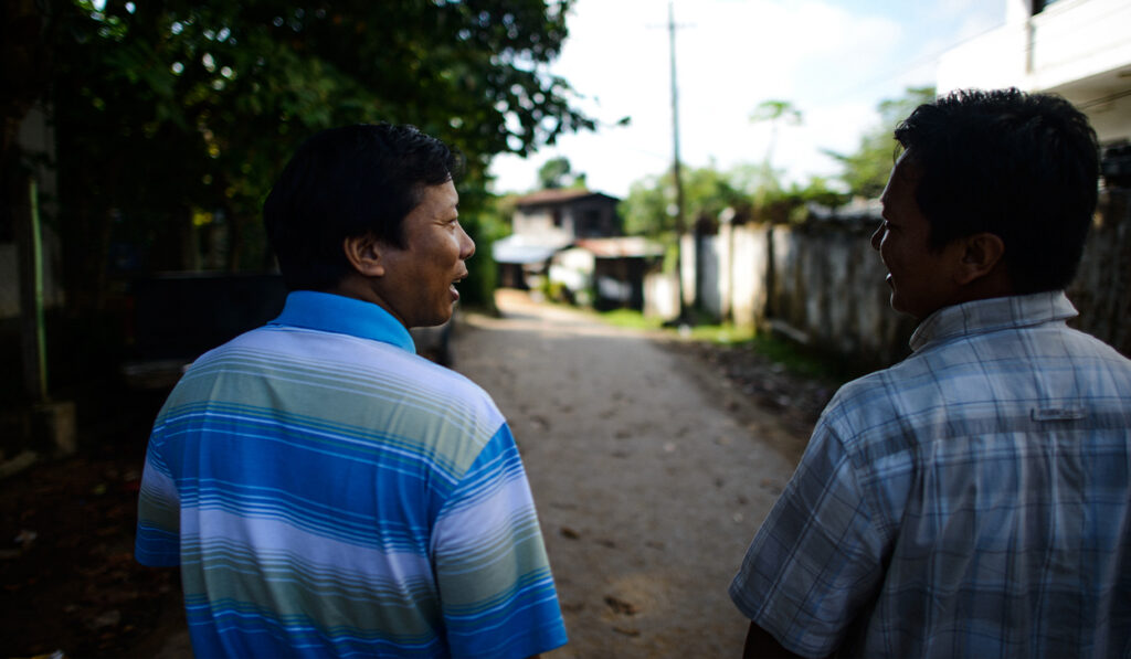Two men in Southeast Asia walk down a dirt road together.