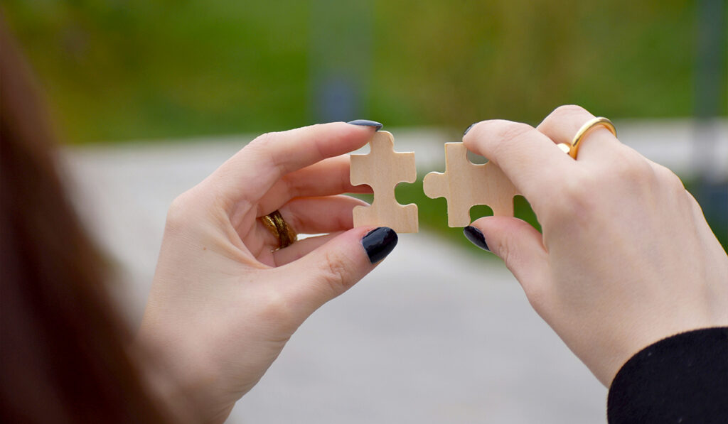 A woman with black nail polish holds up two puzzle pieces.