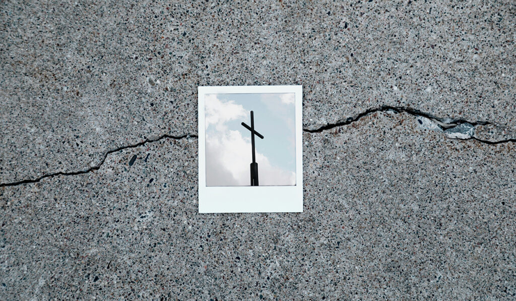 A Polaroid of a cross sits on top of a crack on the sidewalk.