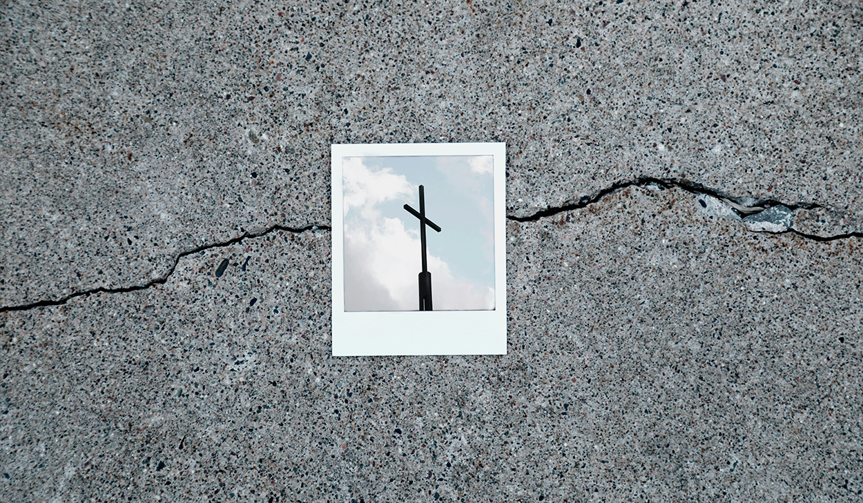 A Polaroid of a cross sits on top of a crack on the sidewalk.