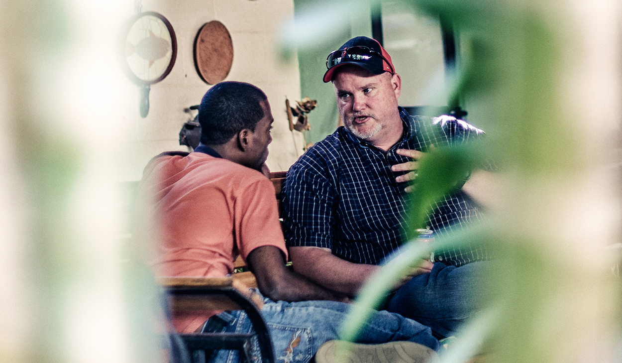 Two men in Latin America are talking and sitting on a porch.