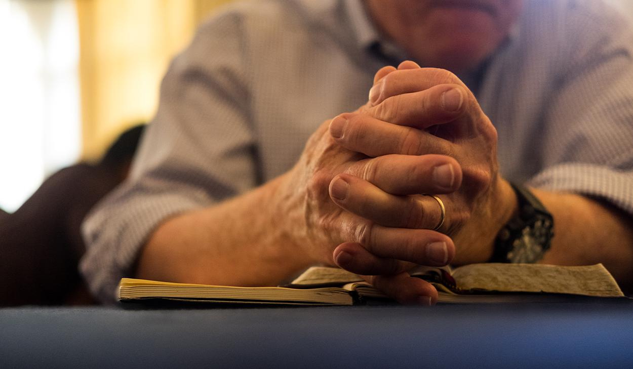 A man rests his folded hands on top of a Bible.