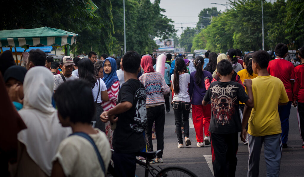 A girl in a pink hijab stares at the camera in the midst of a crowded street.