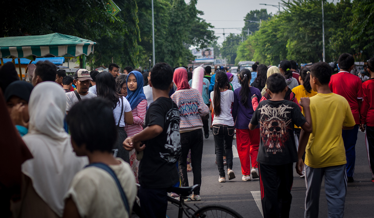 A girl in a pink hijab stares at the camera in the midst of a crowded street.