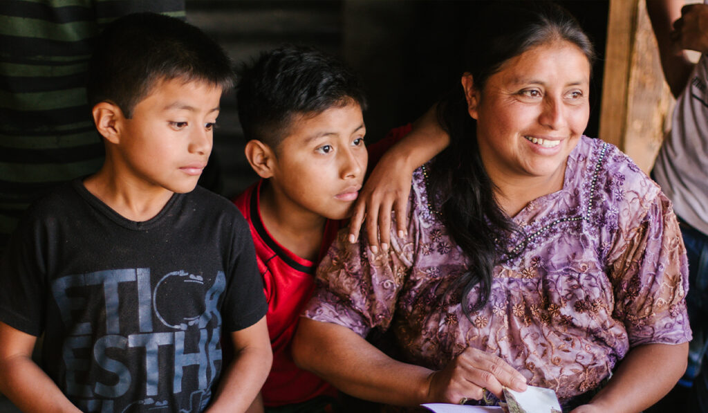 A smiling woman in a purple shirt and two boys look off camera.