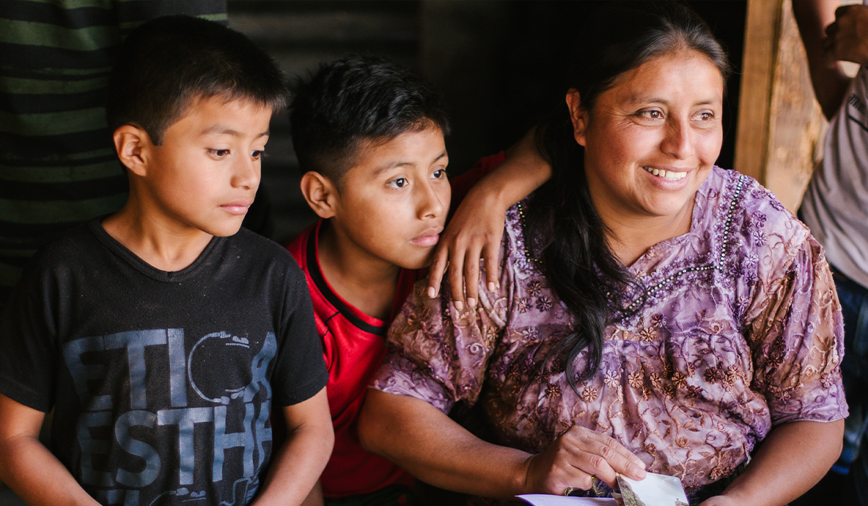 A smiling woman in a purple shirt and two boys look off camera.